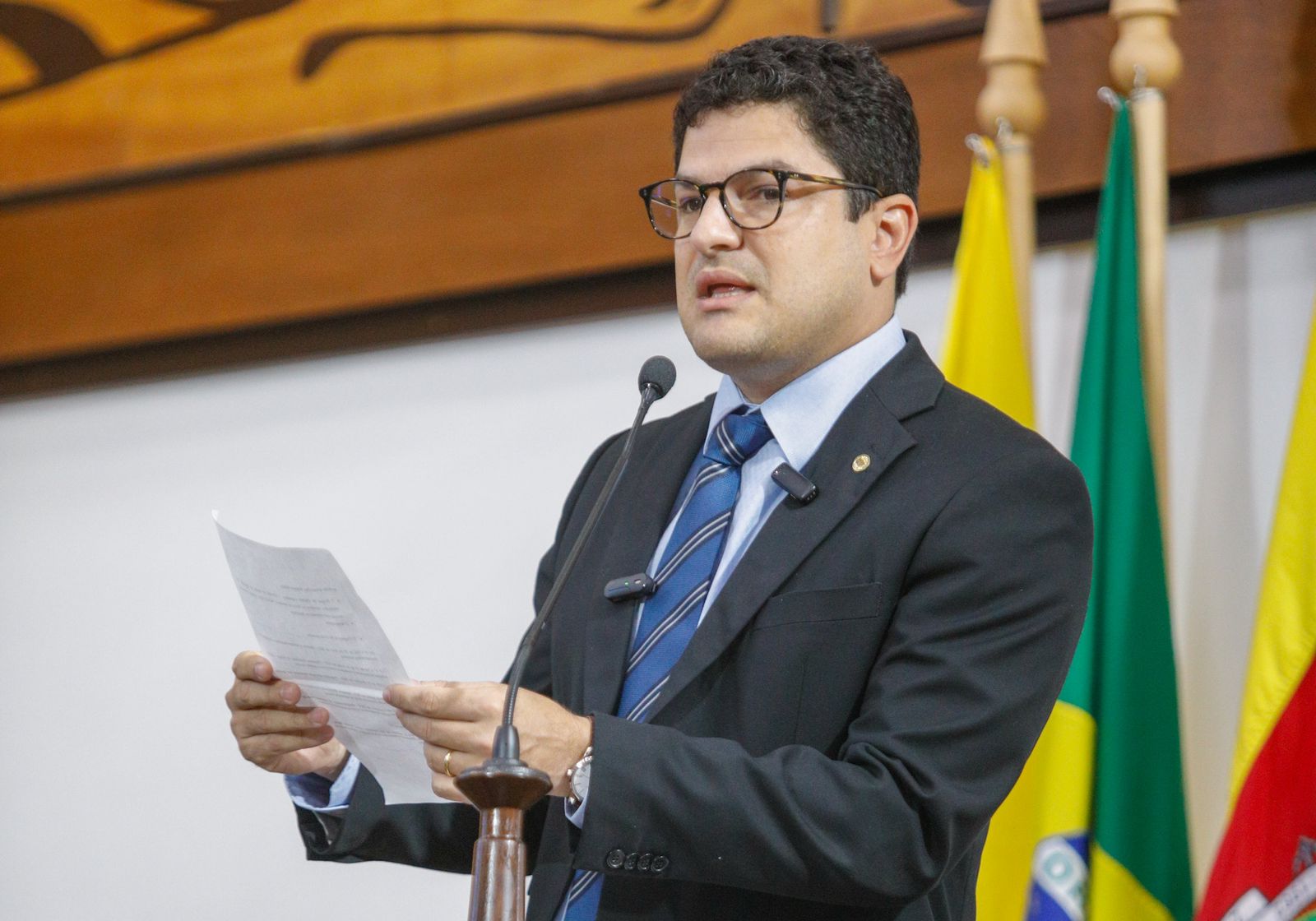 pessoa discursando ao microfone segurando uma folha